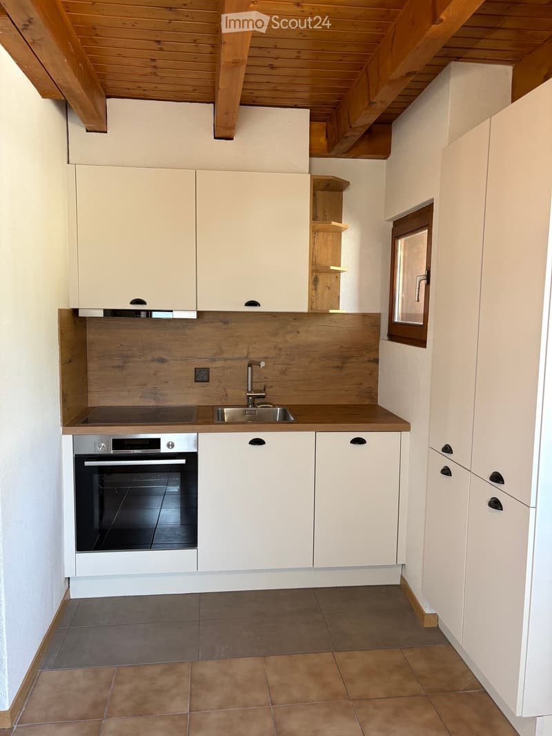 Modern kitchen with white cabinets, wooden countertop, stainless steel sink, and built-in oven. Features exposed wooden beams on the ceiling and a small window.