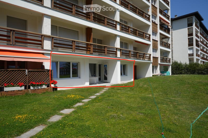 Multi-story residential building with balconies, white exterior, and a well-maintained lawn in front.