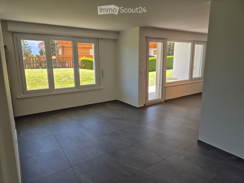 Empty room with dark tiled flooring, large windows, and sliding glass doors leading to an outdoor area.
