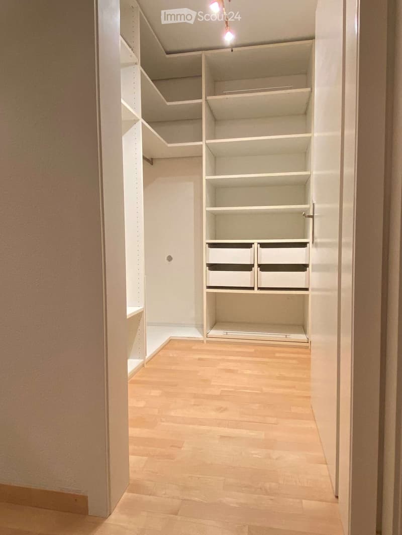 Empty closet with white built-in shelving and drawers, wooden floor, and recessed lighting.