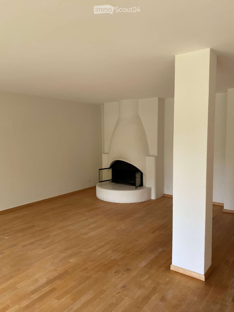 Empty room with light wooden flooring and a white fireplace structure in the center.