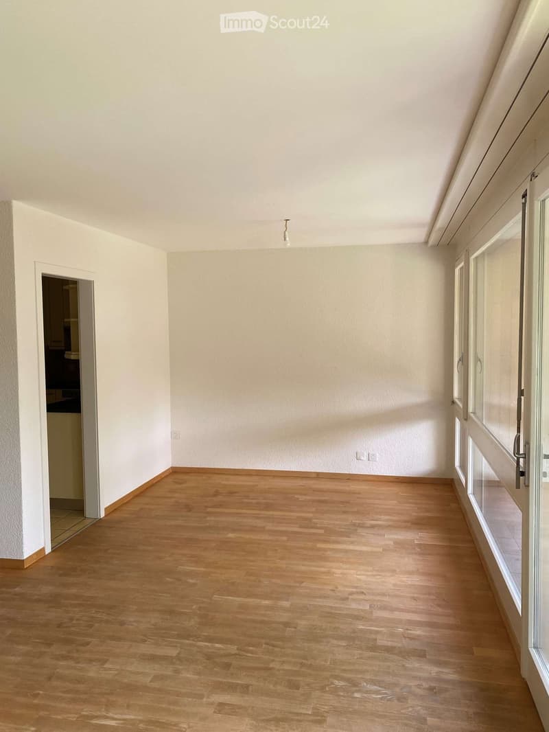 Empty room with light wooden flooring, white walls, and large windows. No furniture or equipment present.