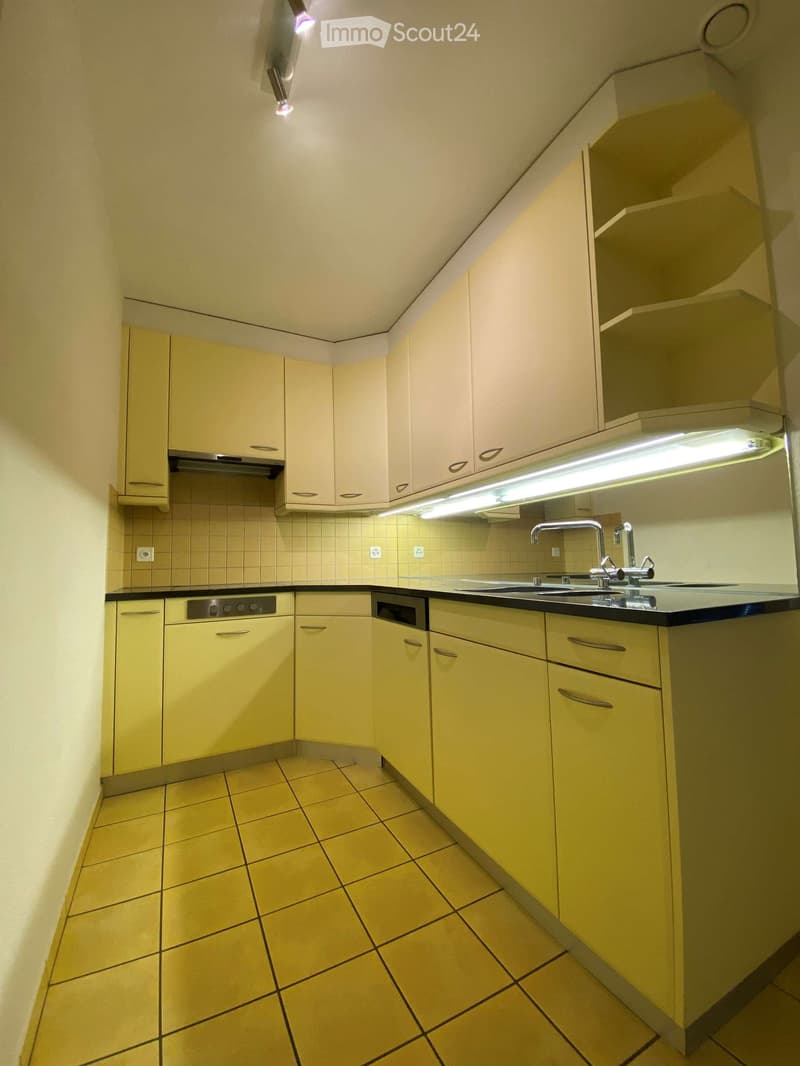 Modern kitchen with light yellow cabinets, tiled floor, and stainless steel appliances including a sink, oven, and dishwasher.