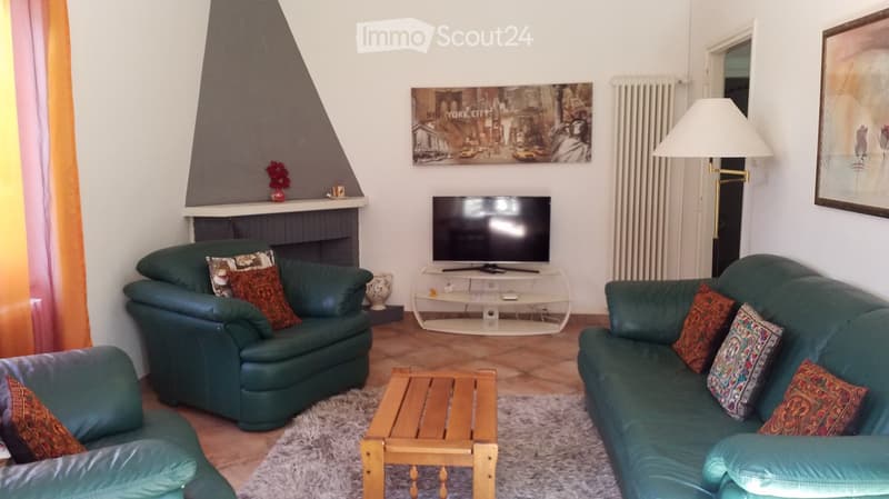 Living room with green leather sofa and armchair, wooden coffee table, television, floor lamp, fireplace with decorative items, and artwork on the wall.