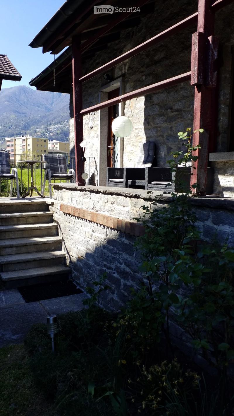 Balcony with stone walls, wooden beams, and a view of the mountains. Includes a wicker sofa, chairs, and a small table.