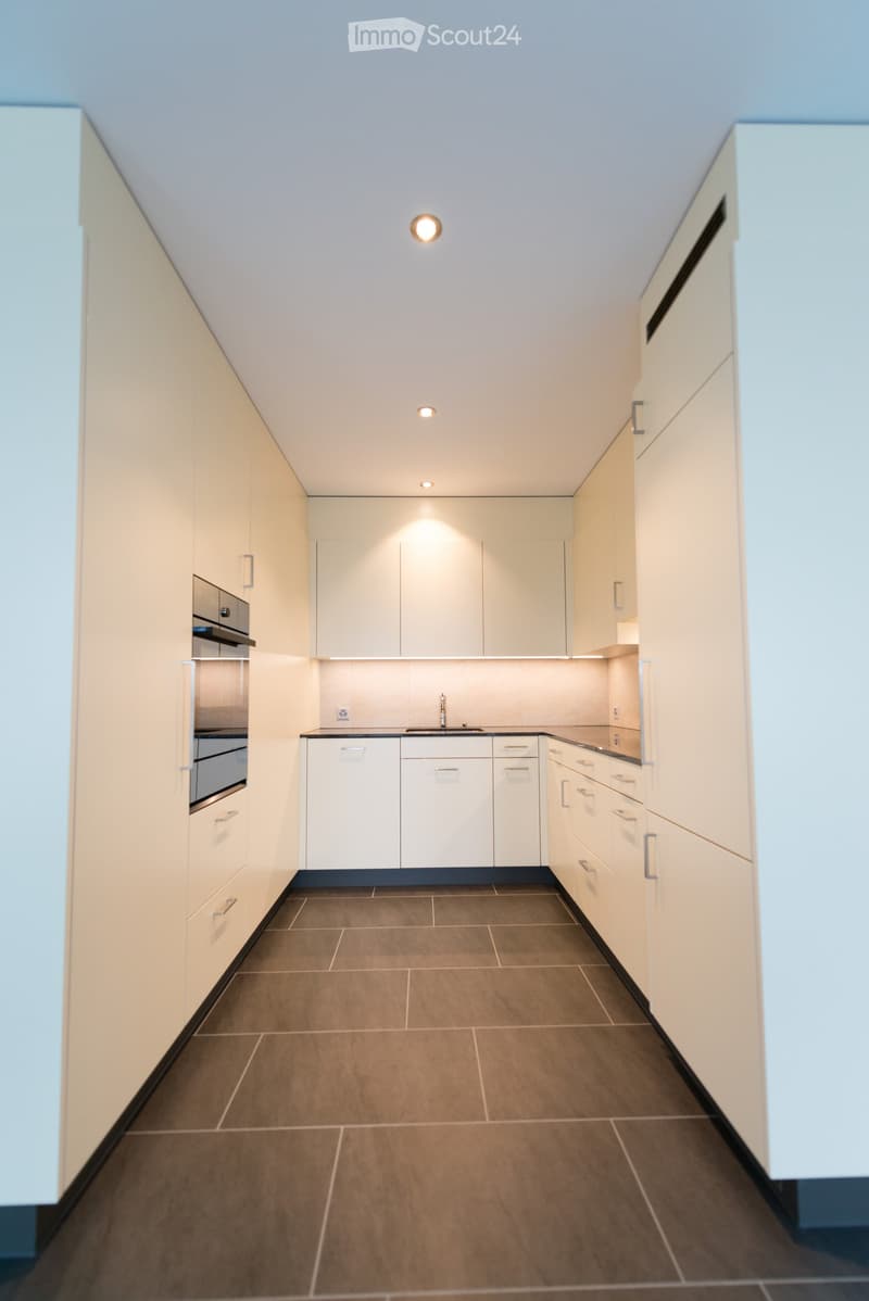 Modern kitchen with white cabinets, dark tiled floor, and stainless steel appliances including a sink and oven.