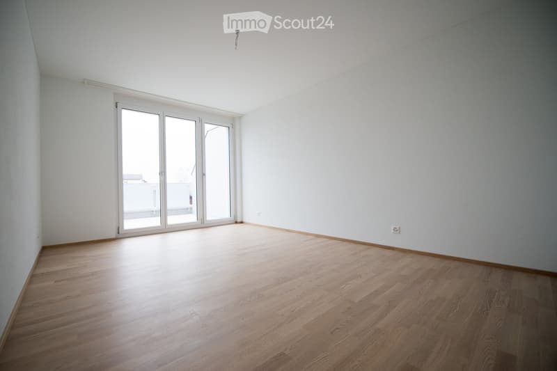 Empty room with light wooden flooring, white walls, and large sliding glass doors leading to a balcony.