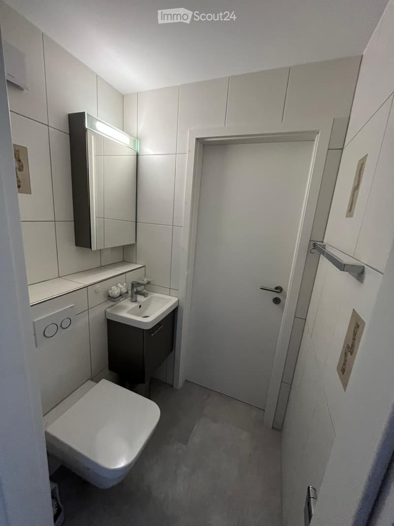 Modern bathroom with white tiles, a toilet, a sink with a mirror, and built-in cabinets.