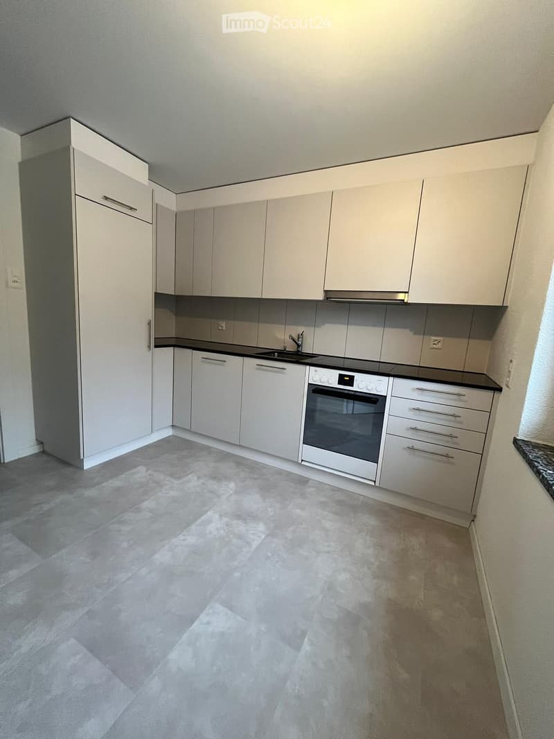 Modern kitchen with white cabinets, stainless steel oven, sink, and faucet, featuring a light grey tiled floor and black countertops.