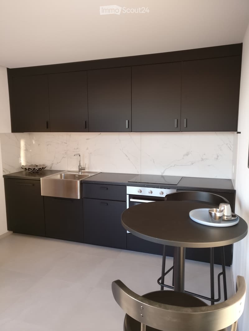 Modern kitchen with dark cabinets, marble backsplash, stainless steel sink, oven, and a small round table with chairs.
