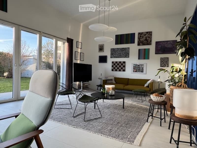 Modern living room with large windows, grey sofa, coffee table, chairs, and decorative artwork on the walls.