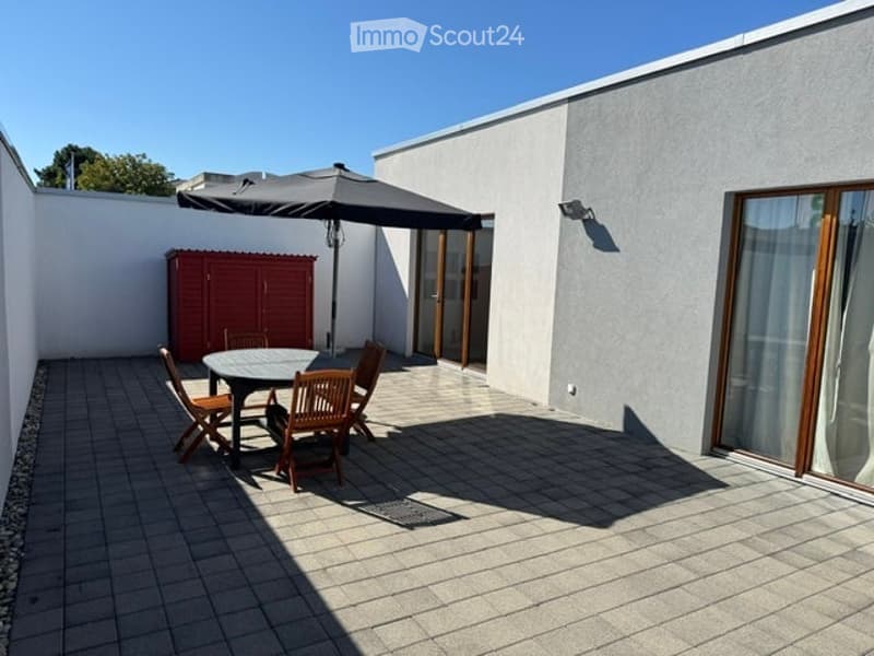 Outdoor patio with tiled floor, round table, four wooden chairs, large umbrella, and red storage cabinet.