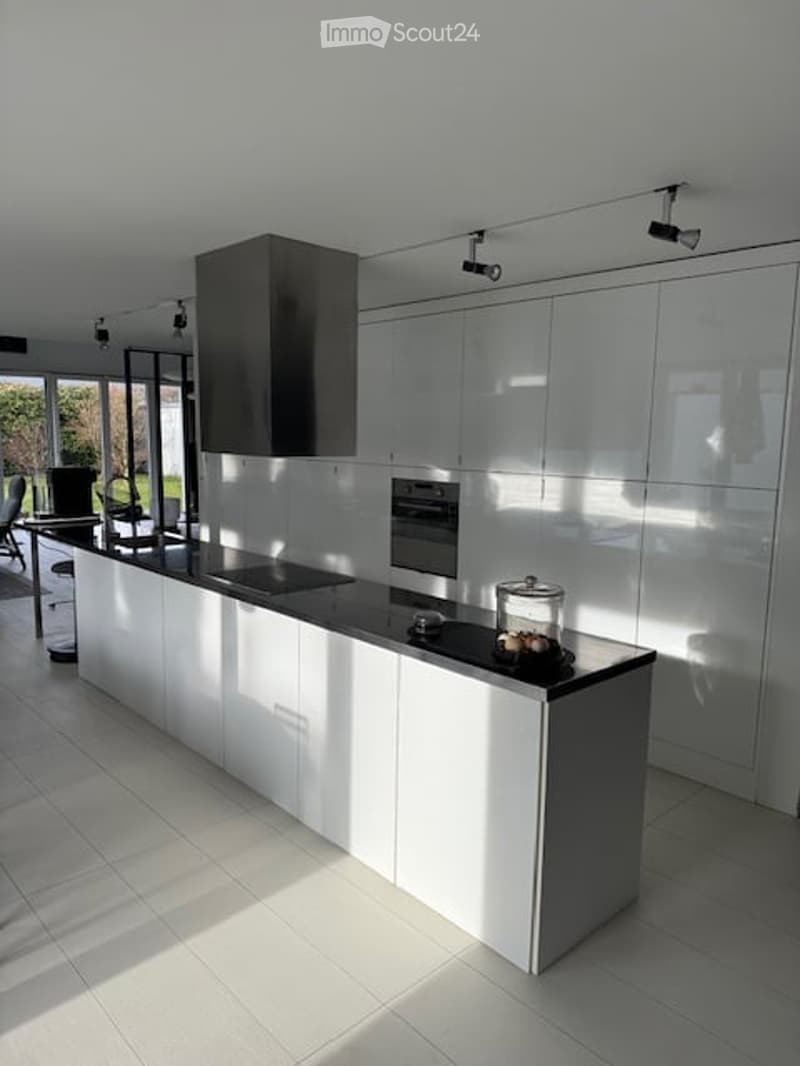 Modern kitchen with white cabinetry, black countertop, built-in oven, range hood, and a small dining area with a table and chairs.