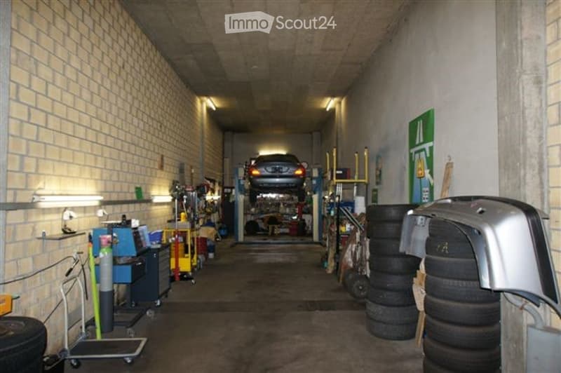 Garage with a car on a lift, shelves with tools, tires stacked, and a green sign on the wall.