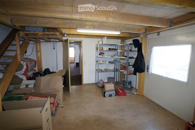 Empty room with exposed wooden beams on the ceiling, concrete floor, metal shelving unit, and scattered boxes and items.