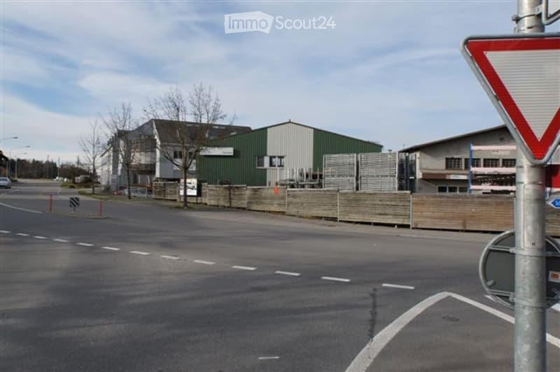 Industrial building with green and white exterior, located near a road with traffic signs and barriers.