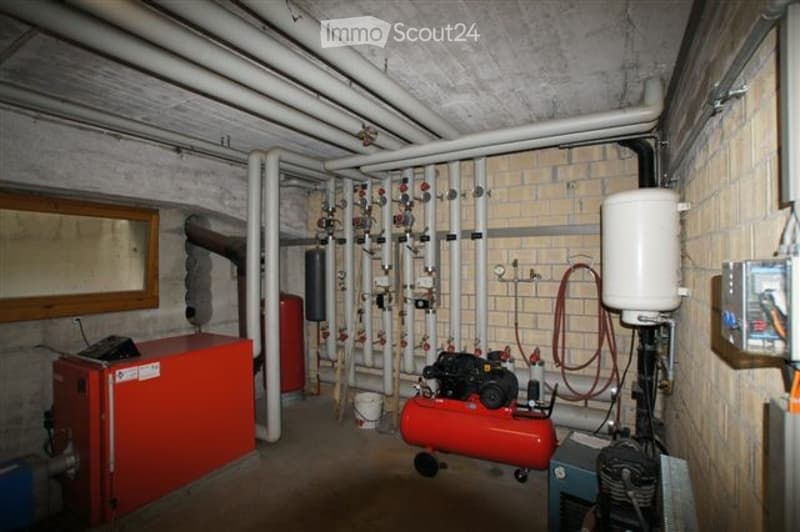 Utility room with exposed pipes, a red compressor, a white boiler, and an electrical panel.