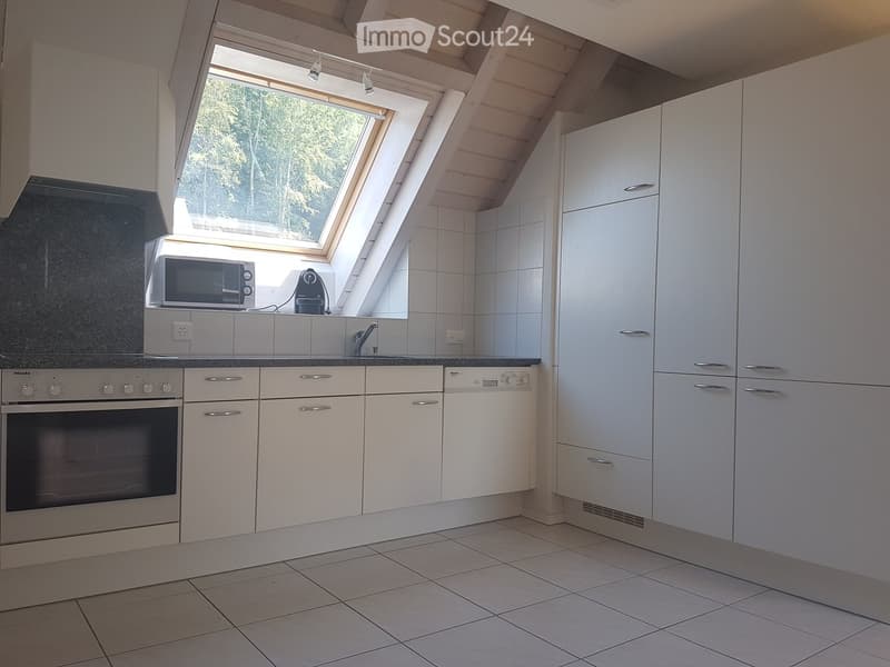 Modern kitchen with white cabinets, tiled floor, and stainless steel appliances including an oven and microwave. Features a skylight window above the sink.