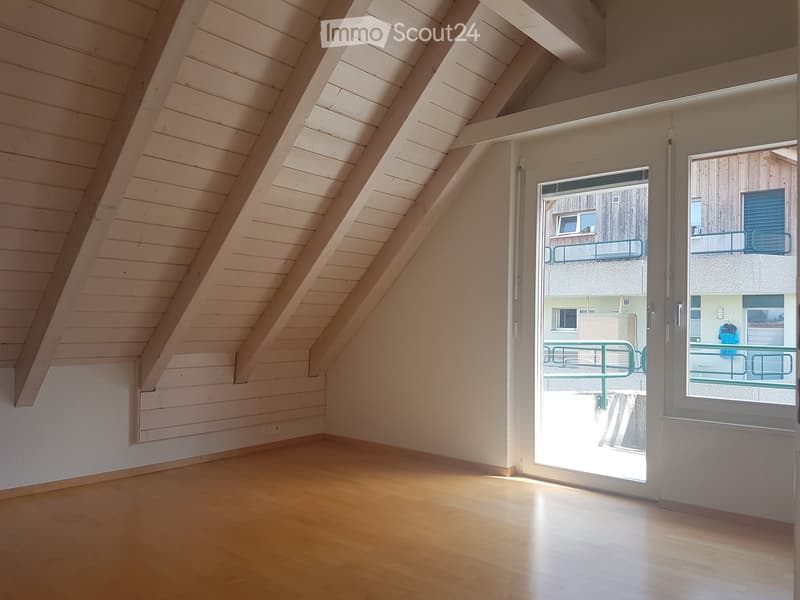 Empty attic room with wooden walls and floor, large skylight, and open door leading to a balcony.