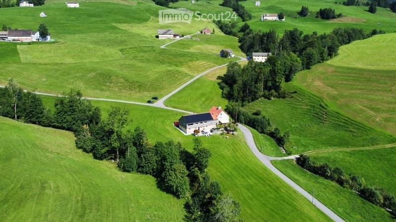 Aerial view of a rural landscape with green fields, scattered houses, trees, and winding roads.