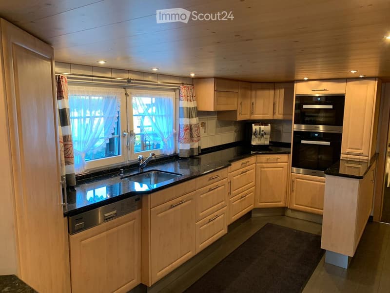 Modern kitchen with light wooden cabinets, black granite countertops, stainless steel appliances, and a window with curtains.