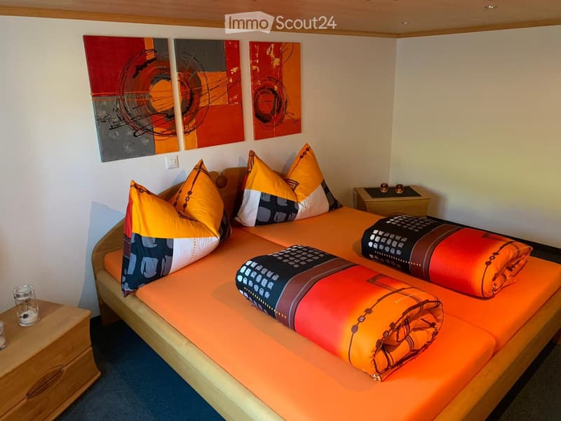 Brightly colored bedroom with a single bed, orange bedding, colorful pillows, and modern artwork on the wall.