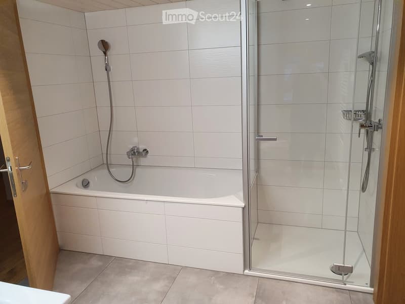 Modern bathroom with a white tiled bathtub, glass-enclosed shower, and chrome fixtures.