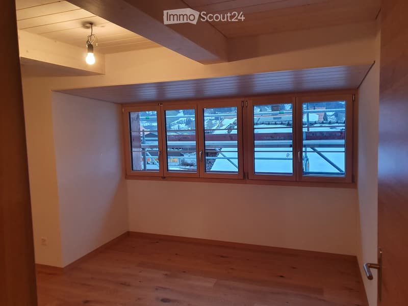 Empty room with wooden flooring, large windows, and a slanted wooden ceiling. Natural light illuminates the space.