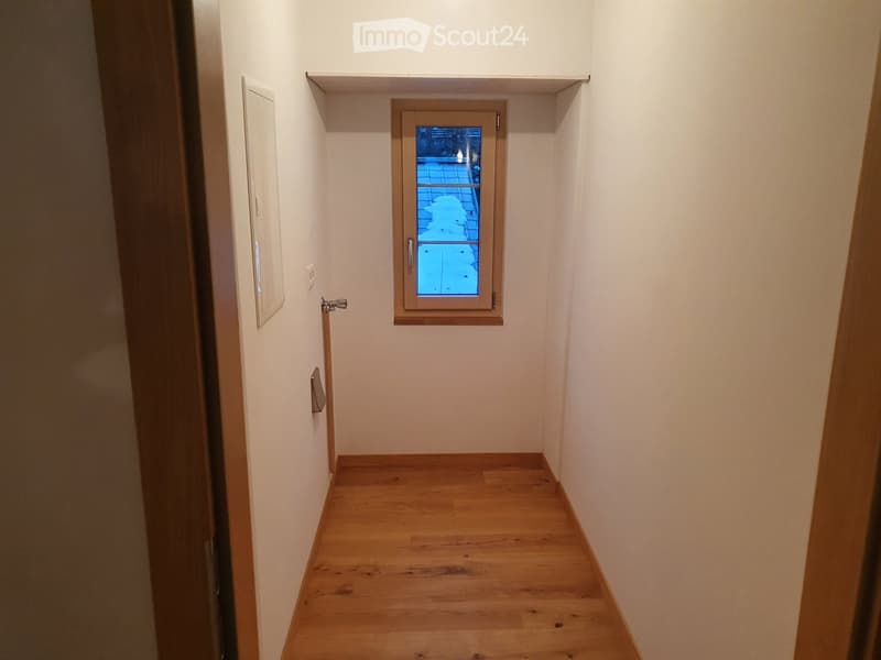 Narrow hallway with wooden flooring, white walls, a small window with a view to an outdoor area, and built-in shelves above the window.