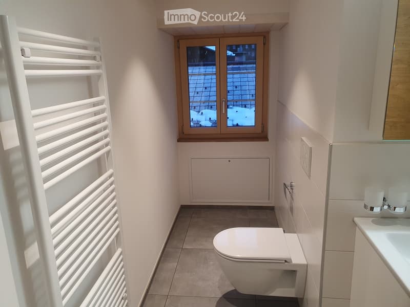 Modern bathroom with white tiled walls, a toilet, a sink with modern faucet, and a white radiator on the left side.