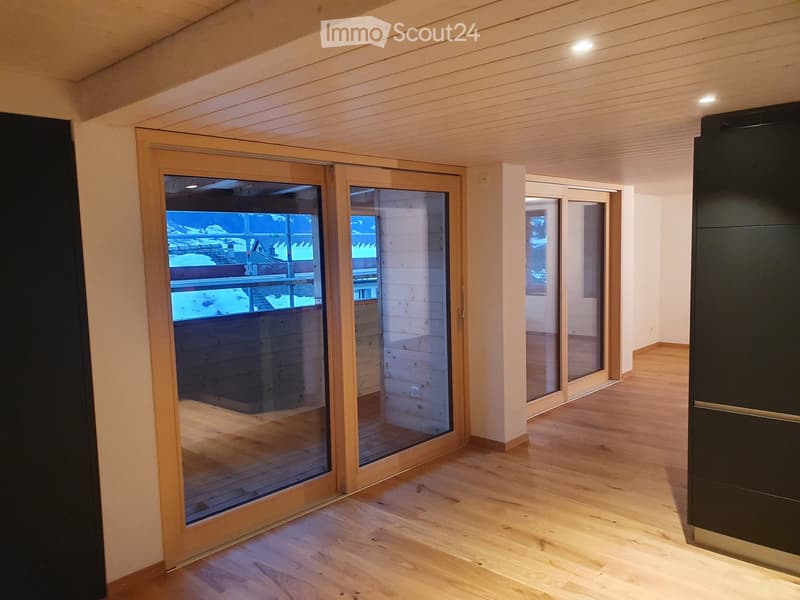 Empty room with wooden flooring, large sliding glass doors leading to a balcony, and a view of the surrounding area.