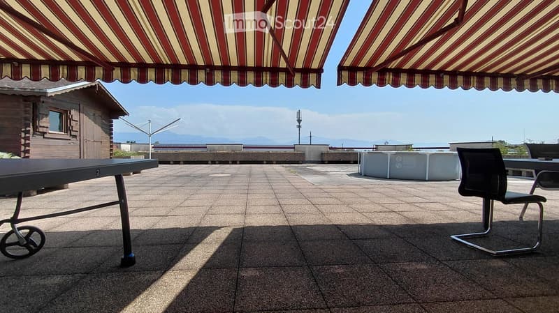 Outdoor terrace with tiled floor, striped awnings, a table and chair, and a view of the sea and mountains.