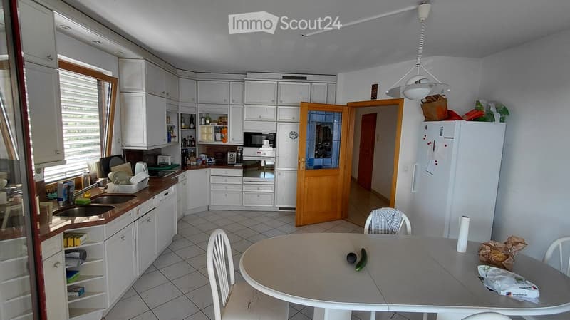 Bright kitchen with white cabinets, tiled floor, and a dining area. Features a sink, fridge, table, and chairs.
