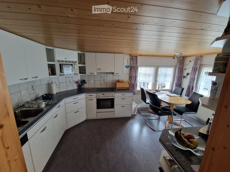 Modern kitchen with white cabinets, stainless steel appliances, and a central island. Features a sink, oven, microwave, and a small dining area with a table and chairs.