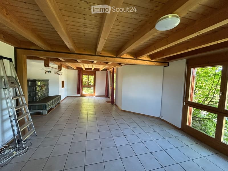 Empty room with wooden ceiling beams, tiled floor, large windows, and a ladder leaning against the wall.