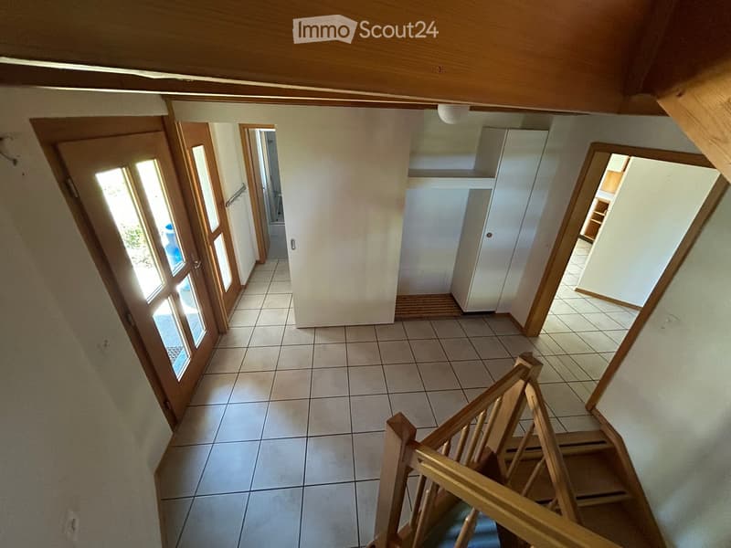 Empty hallway with tiled floor, wooden staircase, and several doors leading to other rooms.