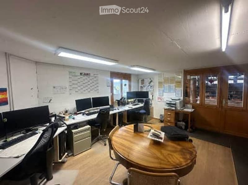 Office space with desks, computers, chairs, a round wooden table, and cabinets.