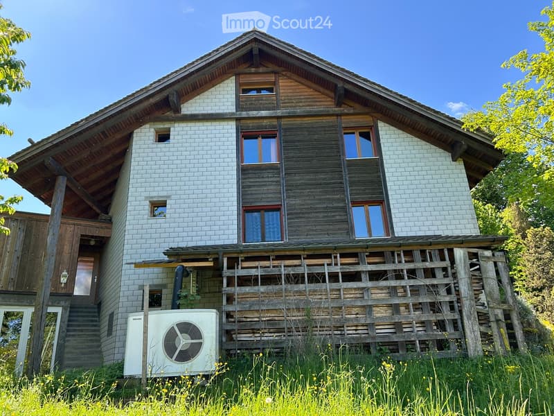 Two-story house with a combination of brick and wooden exterior, multiple windows, and a wooden deck area.