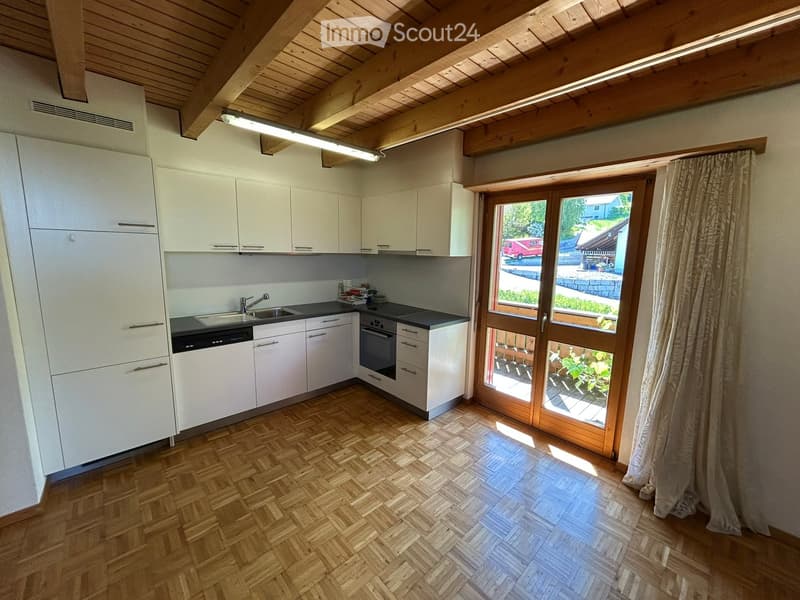 Modern kitchen with white cabinets, wooden herringbone flooring, and a large window with a view of the outdoor area.