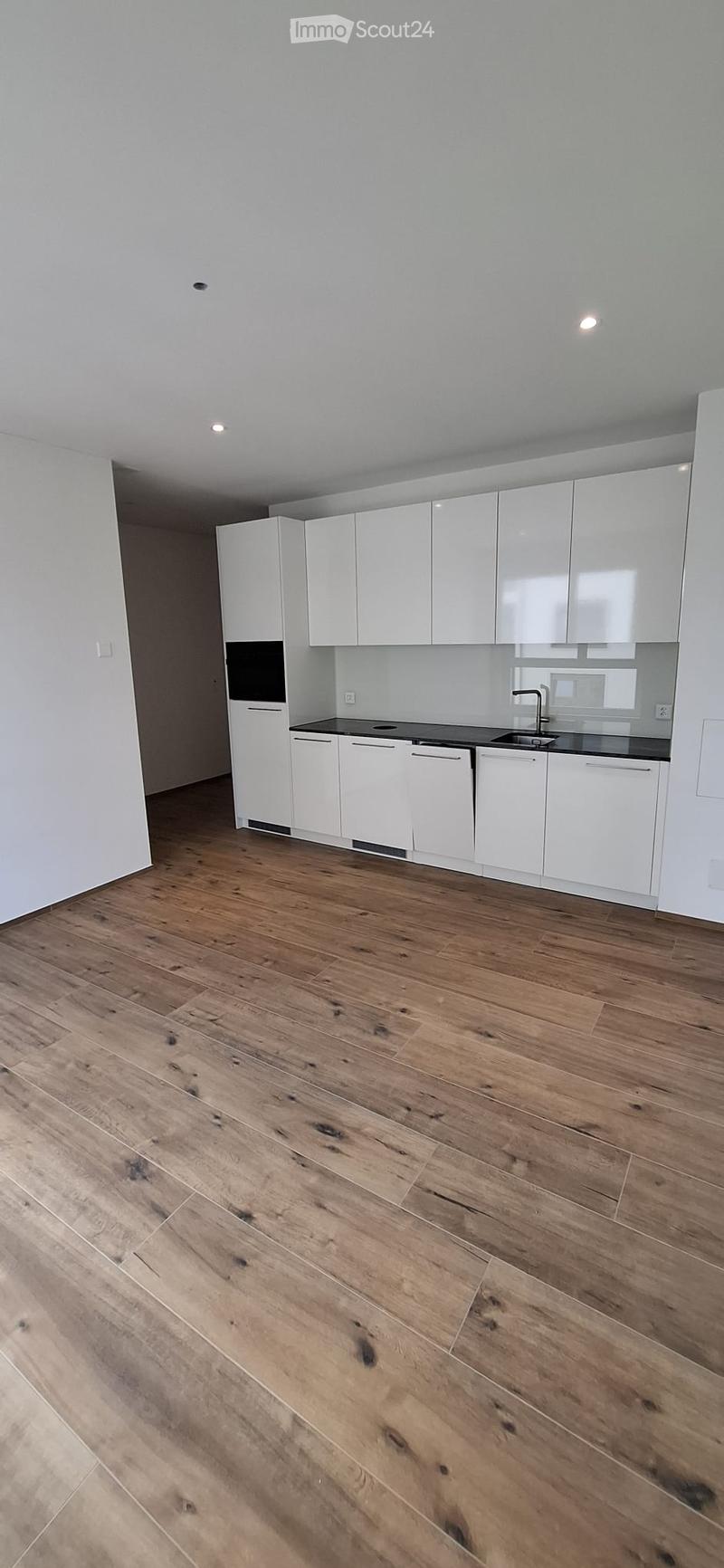 Empty kitchen with white cabinets, dark countertop, and wooden flooring.