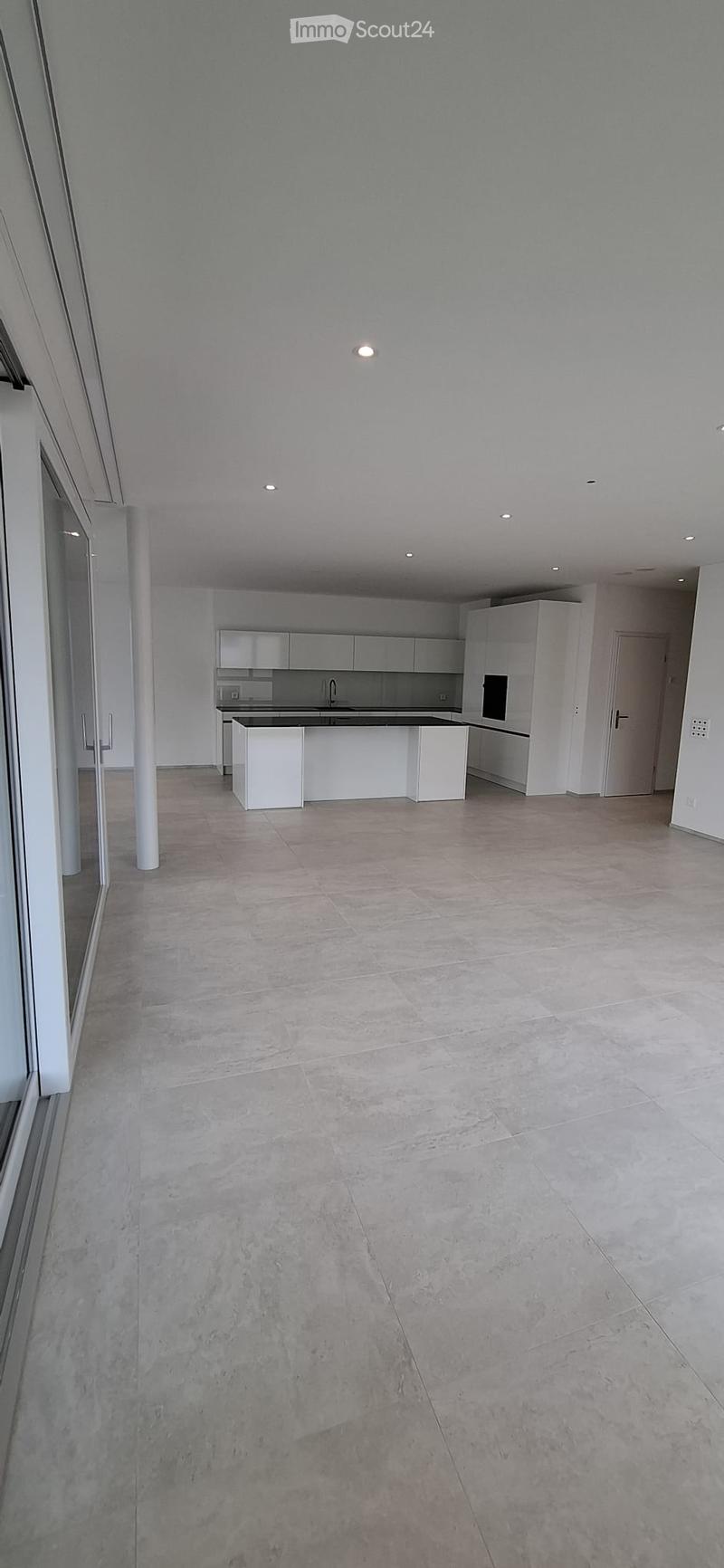 Empty kitchen with white cabinets, a central island, and a tiled floor. No furniture or appliances are present.