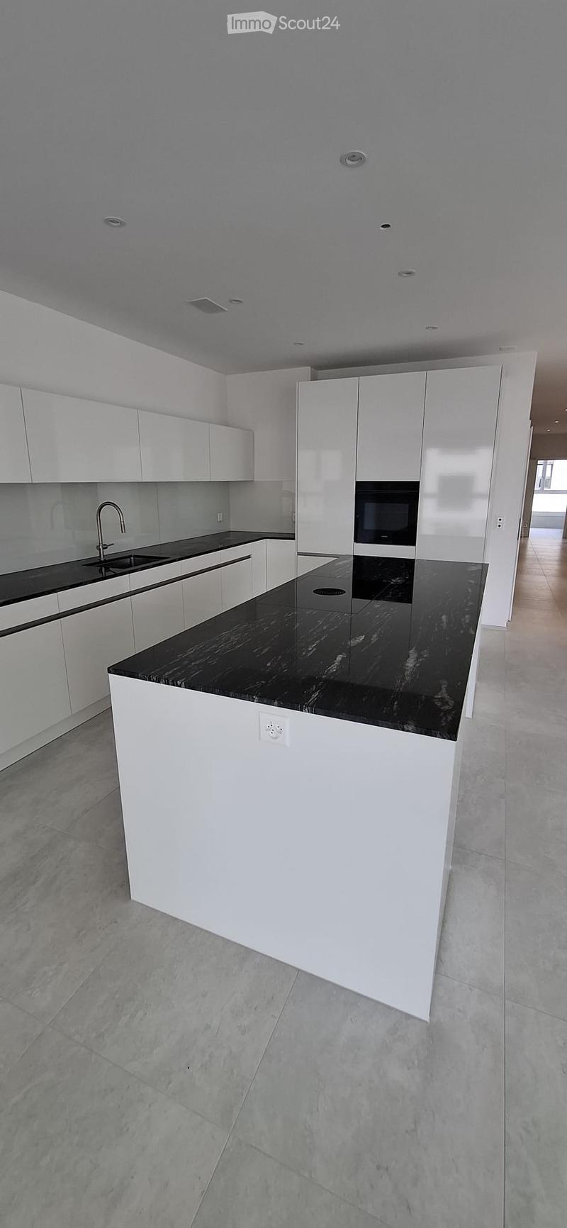 Modern kitchen with white cabinets, black countertops, and a central island. Features a sink with a modern faucet and an integrated oven.