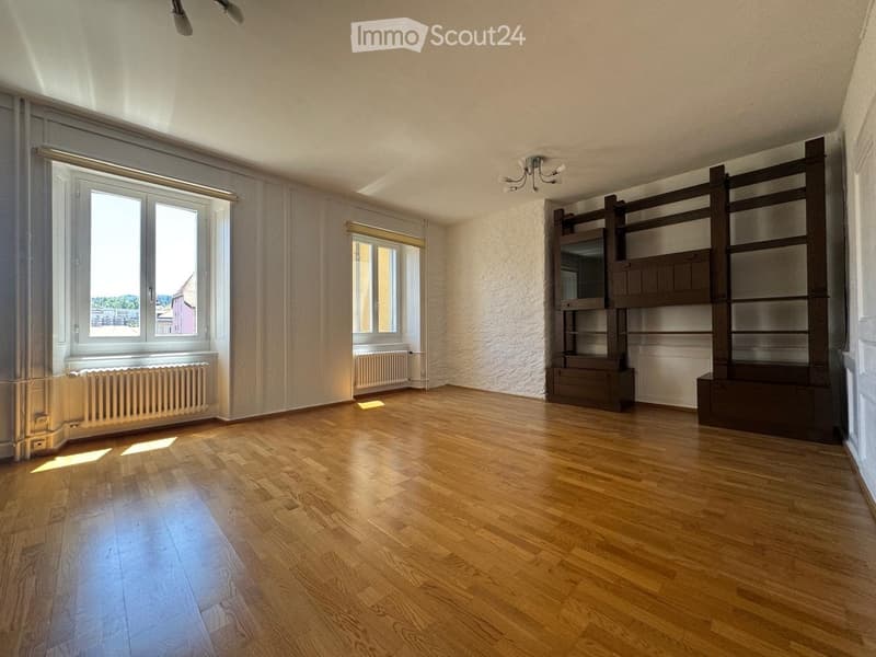 Empty room with wooden flooring, large windows, built-in shelving unit, and radiators.
