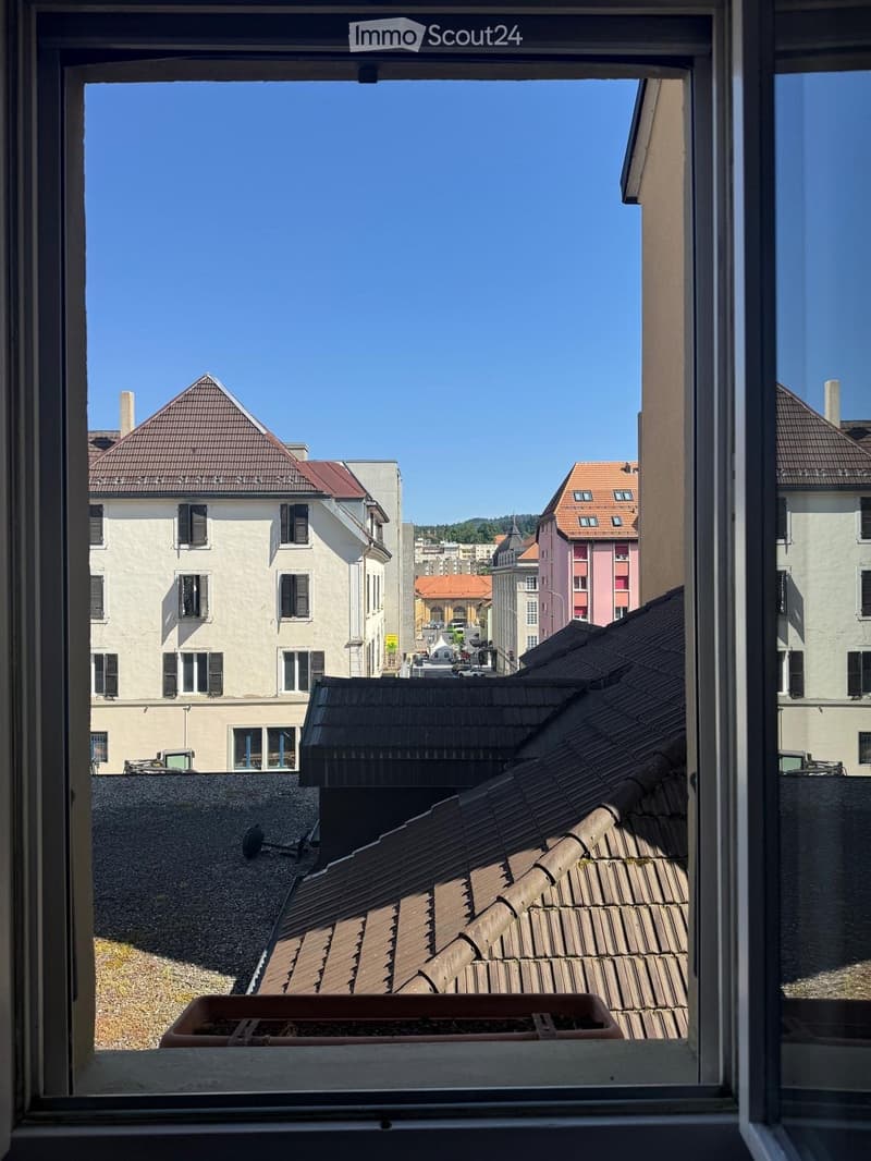 View from a window showing a cityscape with various buildings, rooftops, and a clear blue sky.