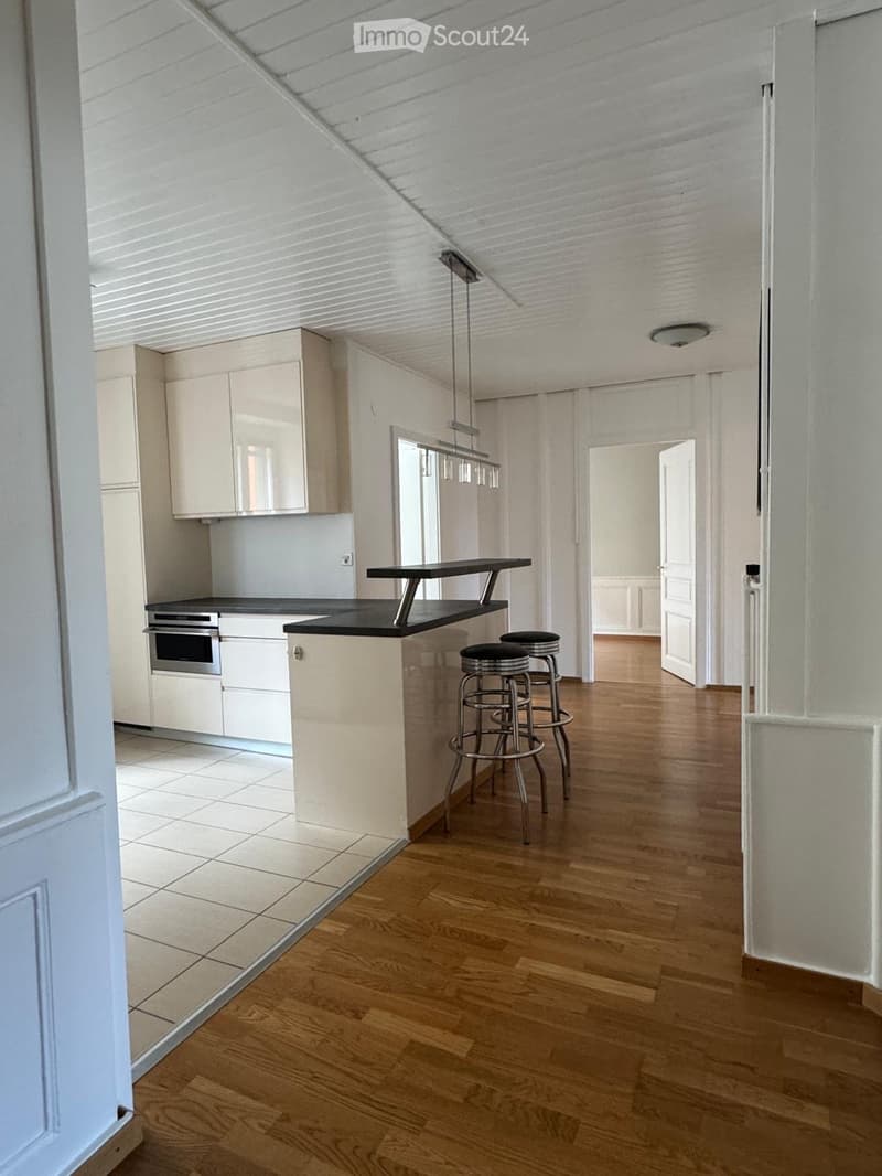 Modern kitchen with white cabinets, a black countertop, and a kitchen island with stools. The space features wooden flooring and pendant lighting.