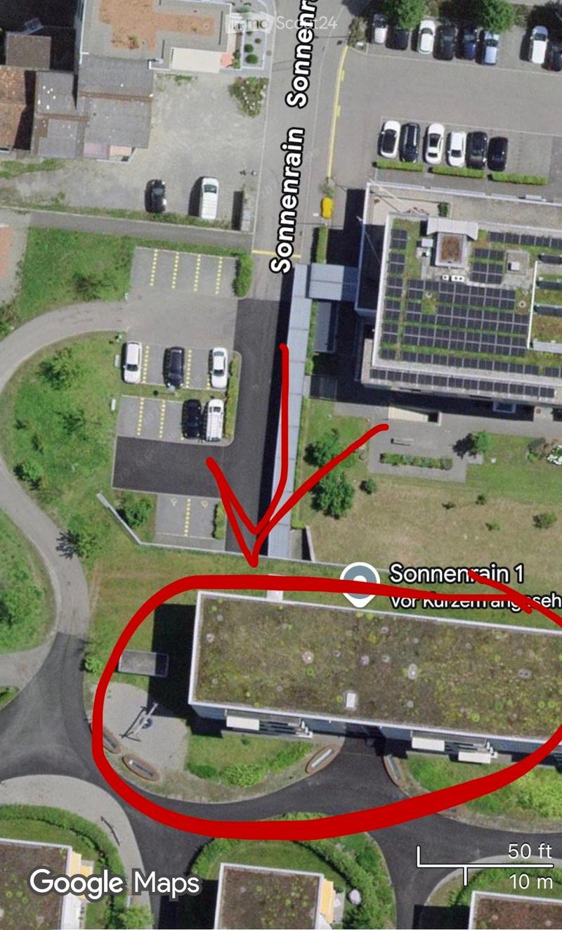 Aerial view of a multi-story building with a parking lot, several parked cars, and a green rooftop area.