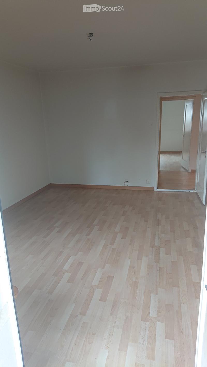Empty room with light wooden flooring and white walls, featuring a doorway leading to another room.