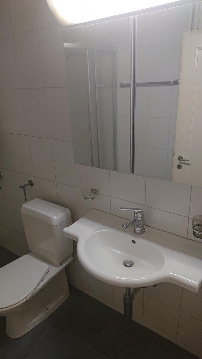 A small bathroom with a white toilet, a white sink with a chrome faucet, and a mirrored cabinet above the sink.