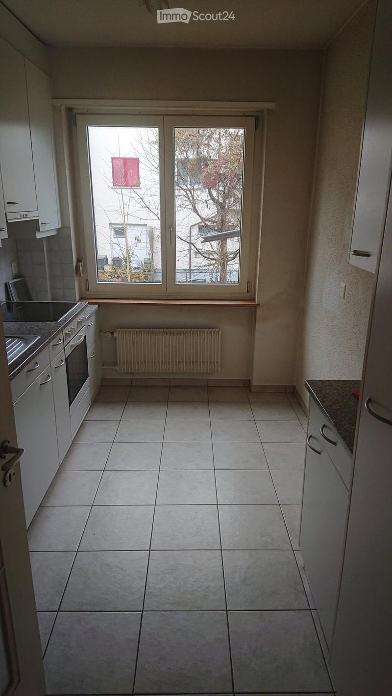 Empty kitchen with tiled floor, white cabinets, a sink, and a window with a view of the outside.