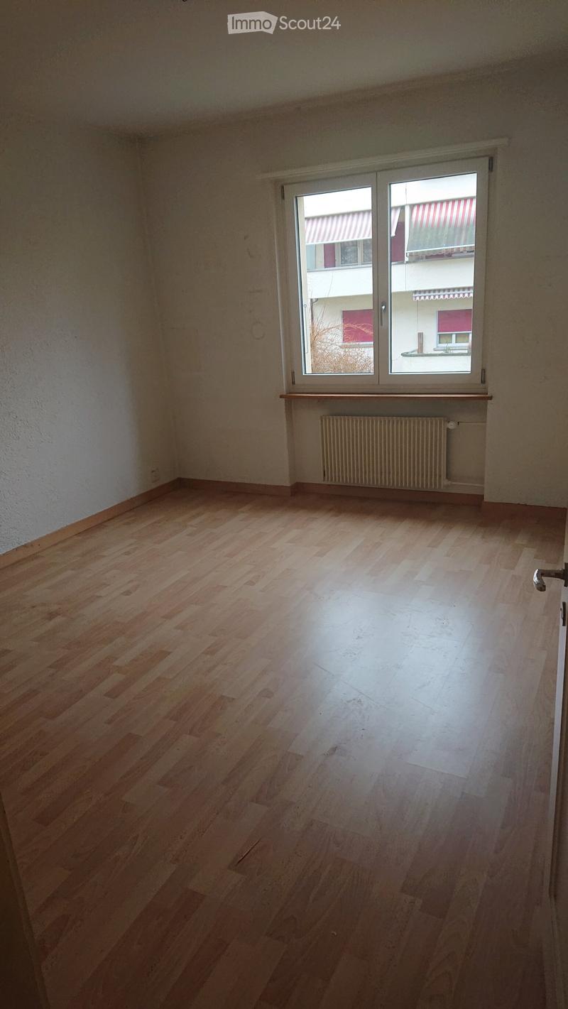 Empty room with wooden flooring, white walls, and a large window with a radiator below it.